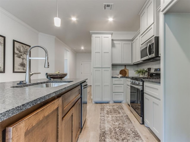 kitchen featuring stainless steel appliances, dark countertops, a sink, and visible vents