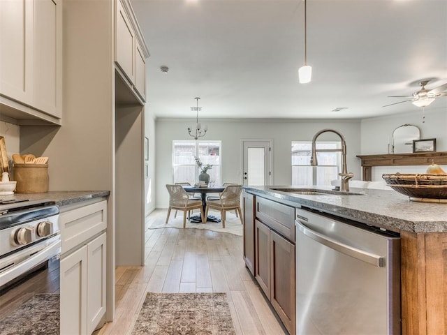 kitchen with light wood-style flooring, decorative light fixtures, light stone countertops, stainless steel appliances, and a sink