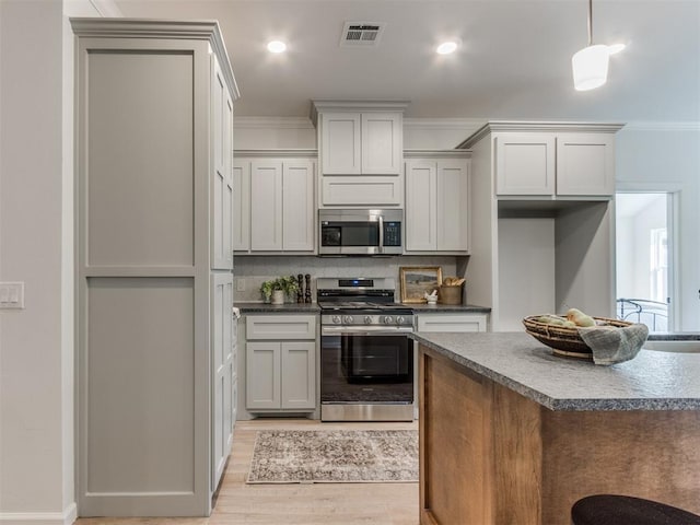 kitchen with crown molding, stainless steel appliances, dark countertops, visible vents, and light wood-style floors