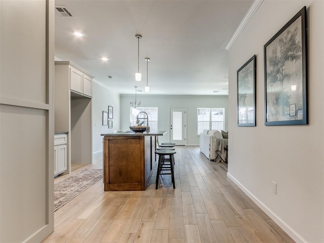 kitchen with a kitchen island with sink, visible vents, baseboards, ornamental molding, and light wood finished floors