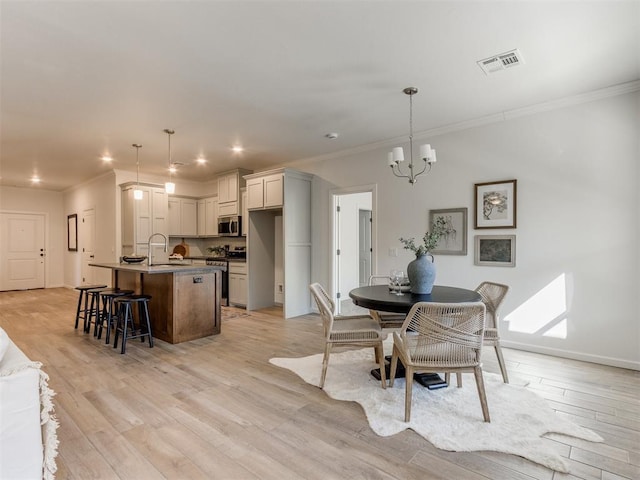 dining room featuring a chandelier, visible vents, baseboards, light wood finished floors, and crown molding