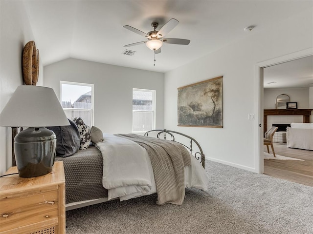 bedroom with baseboards, visible vents, vaulted ceiling, carpet floors, and a fireplace