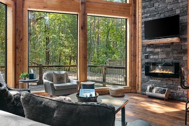 living room with plenty of natural light, wood walls, a stone fireplace, and wood-type flooring