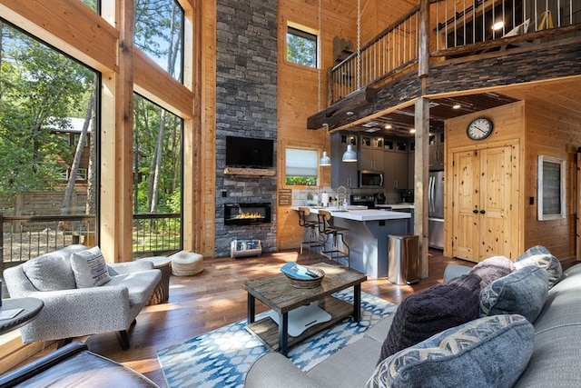 living room featuring a stone fireplace, high vaulted ceiling, a healthy amount of sunlight, and wood walls