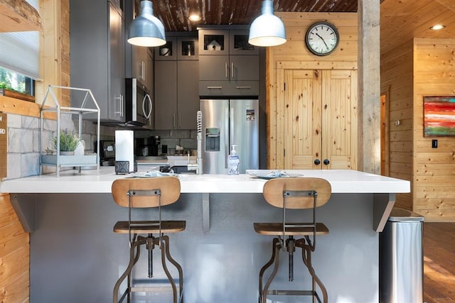 kitchen with a kitchen breakfast bar, wooden walls, pendant lighting, and appliances with stainless steel finishes