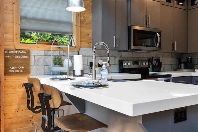 kitchen with kitchen peninsula, a breakfast bar area, appliances with stainless steel finishes, and tasteful backsplash