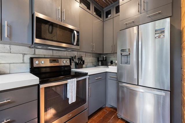 kitchen with dark hardwood / wood-style floors, gray cabinets, appliances with stainless steel finishes, and tasteful backsplash