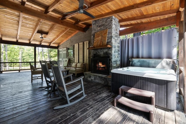 deck with an outdoor stone fireplace, a hot tub, and ceiling fan