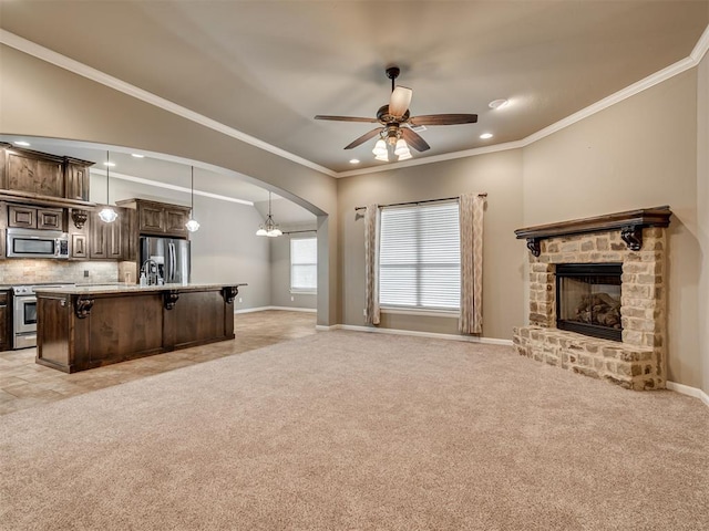 unfurnished living room with light carpet, ceiling fan with notable chandelier, a fireplace, and ornamental molding