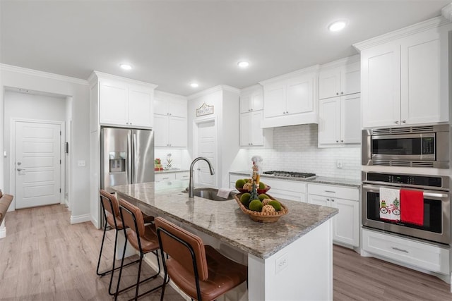 kitchen with white cabinetry, sink, an island with sink, appliances with stainless steel finishes, and light wood-type flooring