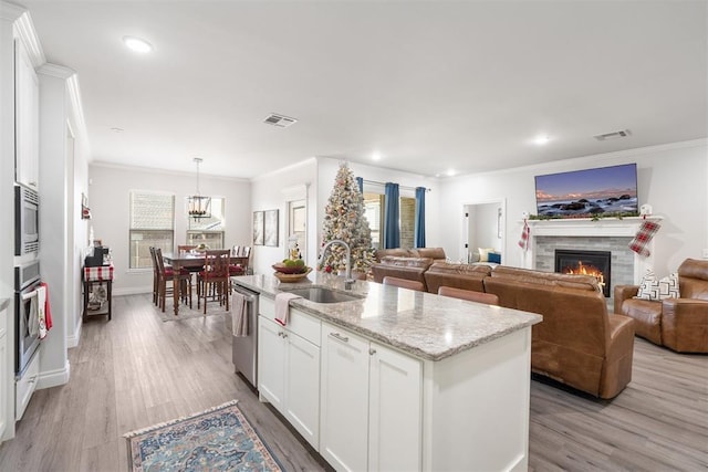 kitchen featuring sink, appliances with stainless steel finishes, a kitchen island with sink, white cabinets, and light wood-type flooring