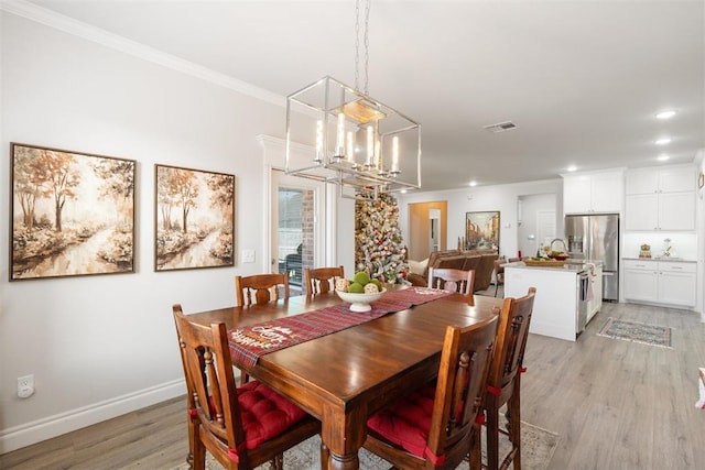 dining room featuring light wood-type flooring, crown molding, and an inviting chandelier