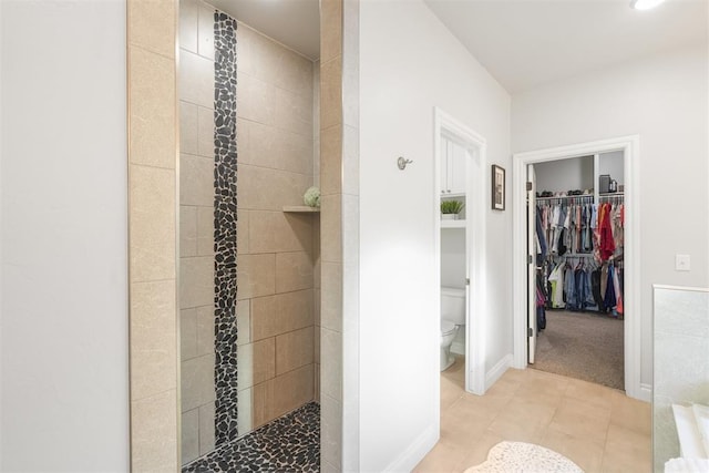 bathroom with toilet, tile patterned flooring, and tiled shower