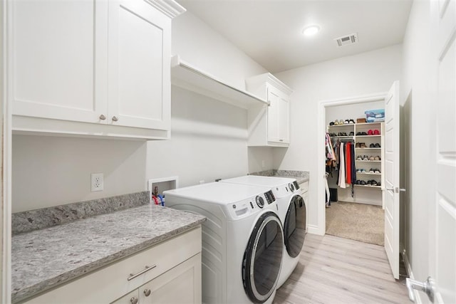 washroom with washing machine and clothes dryer, light hardwood / wood-style flooring, and cabinets