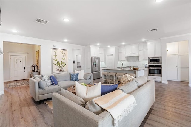 living area featuring recessed lighting, visible vents, ornamental molding, and light wood finished floors