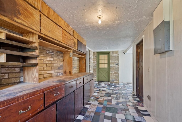 corridor with electric panel, brick wall, and a textured ceiling