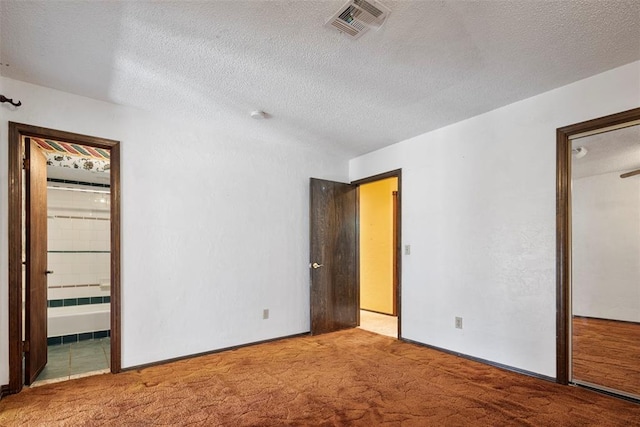 unfurnished bedroom featuring a textured ceiling, connected bathroom, and light colored carpet