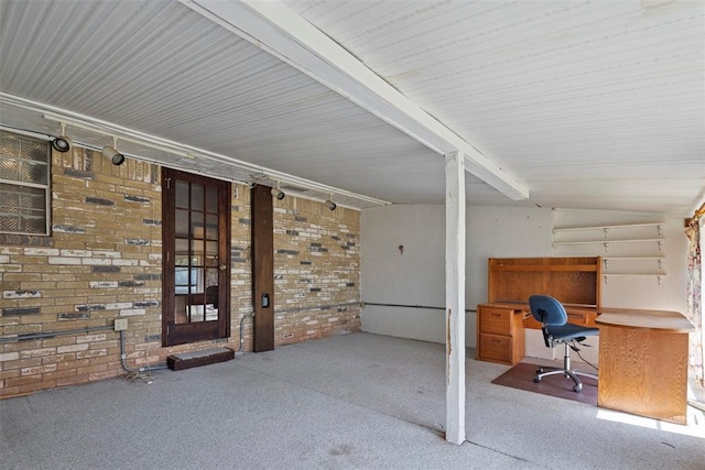 interior space featuring carpet, rail lighting, brick wall, and vaulted ceiling