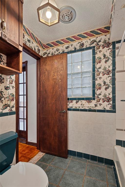 bathroom featuring a textured ceiling, a bathtub, toilet, and tile walls