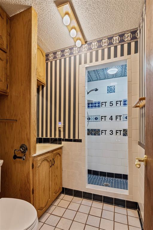 bathroom with a tile shower, tile patterned floors, a textured ceiling, toilet, and vanity