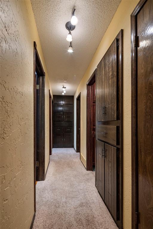 corridor with light colored carpet and a textured ceiling