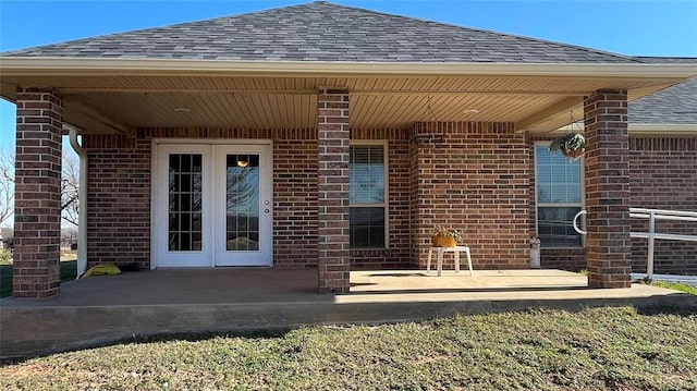 view of exterior entry featuring a patio, brick siding, and roof with shingles