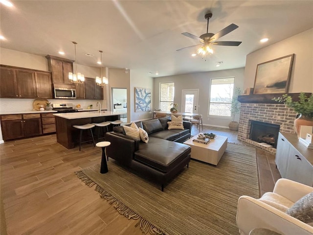 living room with ceiling fan, dark hardwood / wood-style flooring, sink, and a brick fireplace