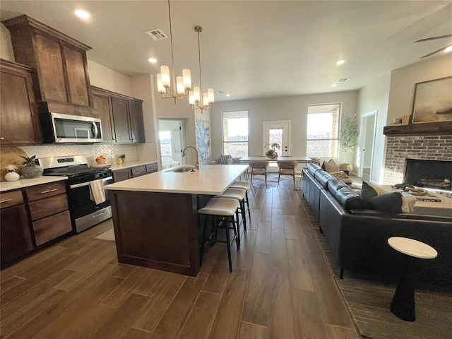 kitchen with stainless steel appliances, light countertops, a sink, an island with sink, and a kitchen breakfast bar