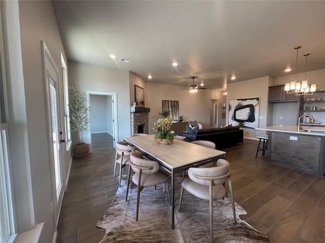 dining room featuring dark wood finished floors, recessed lighting, visible vents, a brick fireplace, and ceiling fan with notable chandelier