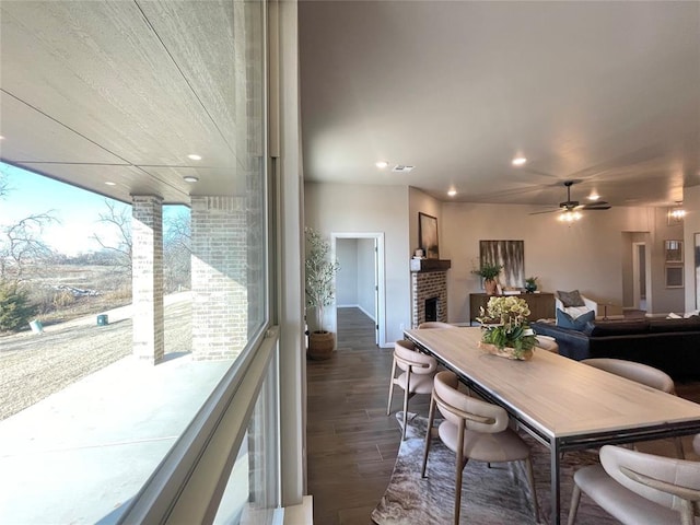 dining space with ceiling fan, dark hardwood / wood-style floors, and a brick fireplace