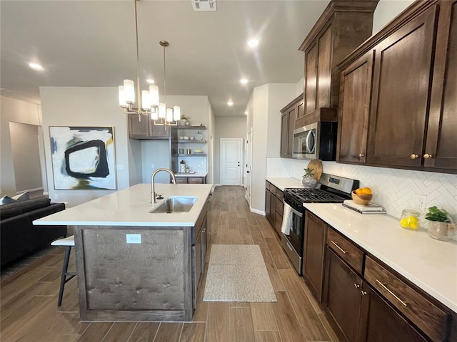 kitchen with stainless steel appliances, a sink, light countertops, decorative backsplash, and decorative light fixtures