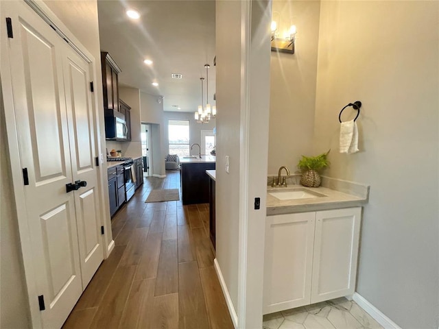 hall with recessed lighting, light wood-type flooring, a sink, and baseboards