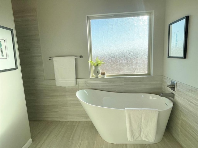 bathroom with a wainscoted wall, a freestanding tub, and tile walls