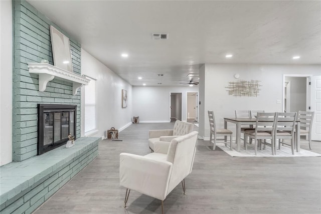 living room with light hardwood / wood-style flooring, a brick fireplace, and ceiling fan