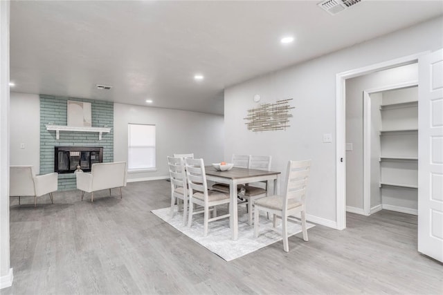 dining space featuring light wood-type flooring and a brick fireplace