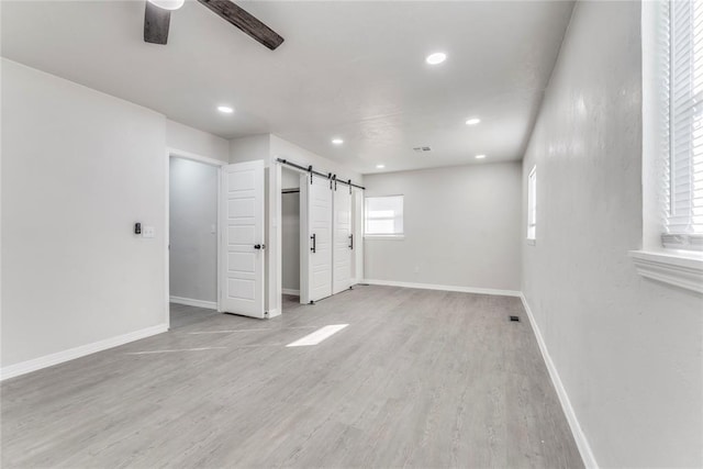 empty room with a barn door, ceiling fan, and light hardwood / wood-style flooring