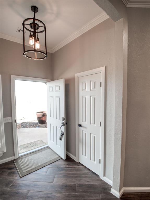 entrance foyer featuring a notable chandelier, crown molding, and dark wood-type flooring