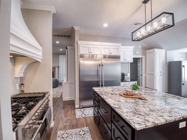 kitchen with high quality appliances, white cabinets, decorative light fixtures, dark hardwood / wood-style flooring, and custom range hood