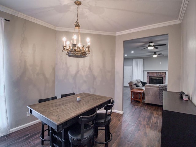 dining area featuring ornamental molding, ceiling fan with notable chandelier, a brick fireplace, and dark wood-type flooring