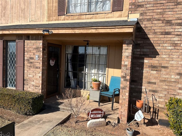 doorway to property with a shingled roof and brick siding