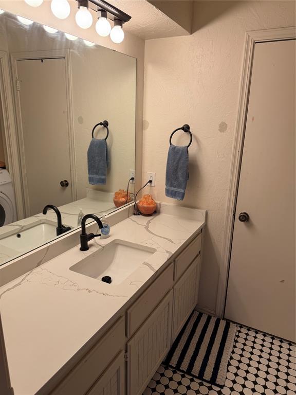 bathroom featuring washer / dryer, a textured wall, vanity, and a textured ceiling