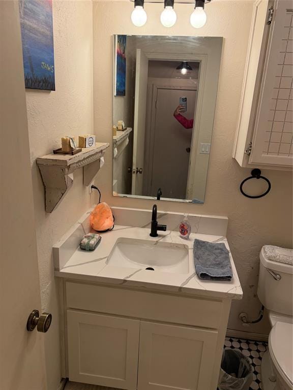 half bathroom with a textured wall, vanity, and toilet