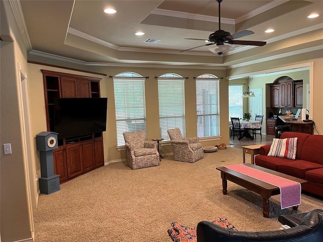 living room with a raised ceiling, light carpet, ceiling fan, and ornamental molding