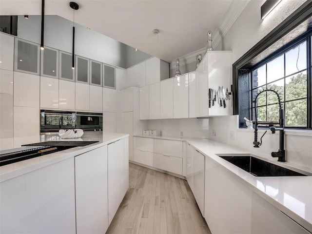 kitchen with white cabinetry, sink, hanging light fixtures, tasteful backsplash, and light hardwood / wood-style flooring