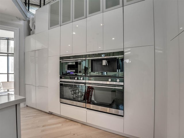 kitchen featuring light wood-type flooring, white cabinetry, double oven, and stainless steel double oven