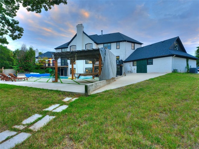 back house at dusk with a pergola, a patio, a yard, and a covered pool