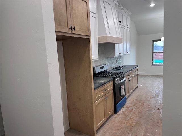 kitchen with light wood-type flooring, tasteful backsplash, stainless steel gas range, custom exhaust hood, and light brown cabinets