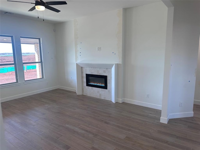 unfurnished living room with dark wood-style flooring, a glass covered fireplace, visible vents, and baseboards