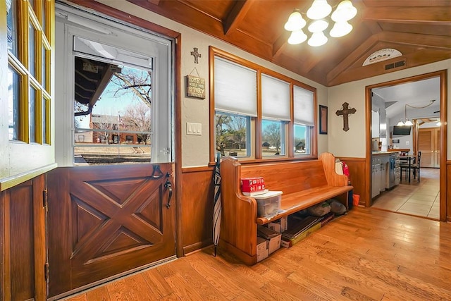 interior space with a notable chandelier, wood walls, lofted ceiling, and light hardwood / wood-style flooring