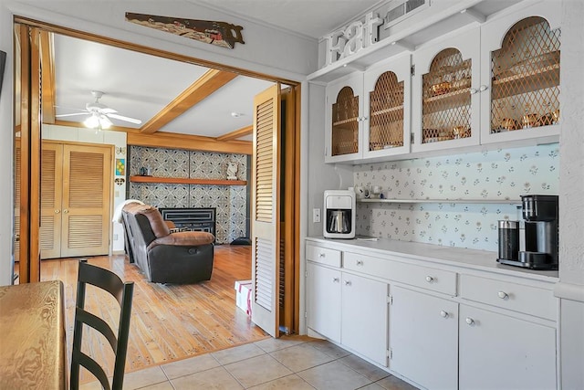 bar featuring a tile fireplace, ceiling fan, white cabinets, and light tile patterned floors